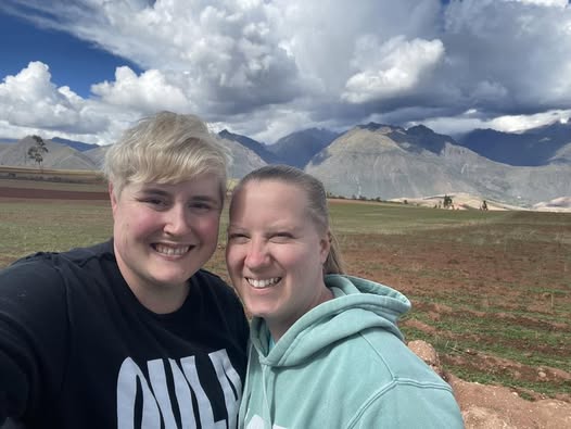 Sara and her wife pose in front of a dramatic cloudscape