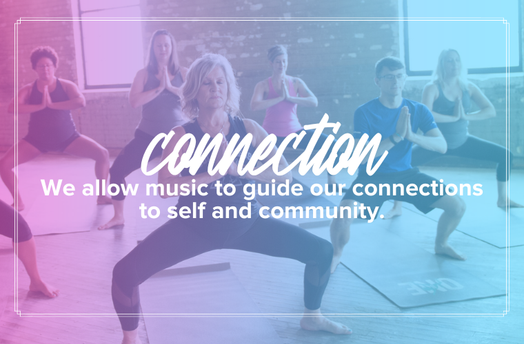 connection: We allow music to guide our connections to self and community. A group of people in a warehouse with yoga mats holding in a wide leg goddess pose, hands together at their hearts.